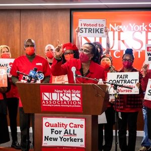 Nancy Hagan at podium backed by nurses holding various signs