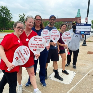 Group of nurses outside hospital hold signs "Nurses Outside = Something's Wrong Inside"