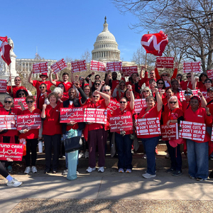 Large group of nurses outside capitol building holding signs "Some Cuts Don't Heal" and "Fund Care Not Billionaires"