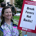 Nurse holds sign "Break fevers not backs"