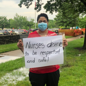 Nurse holds sign "Nurses deserve to be respected and safe"