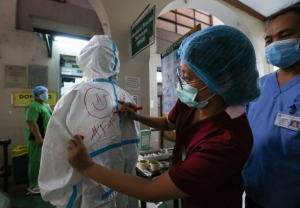 A nurse draws a smiley face on the back of a fellow health worker