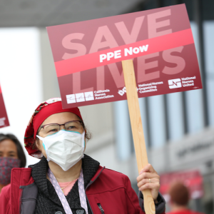 Nurse holds sign "Save Lives, PPE Now"