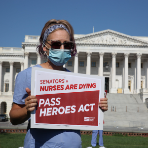 Nurse holds sign outside U.S. Senate "Pass HEROES Act"