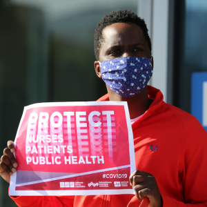 Nurse holds sign "Protect Nurses, Patients, Public Health"