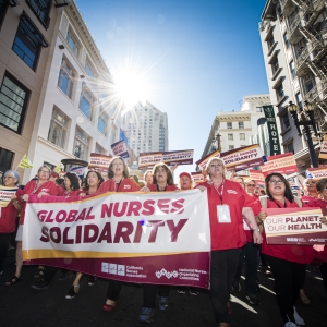 Nurses marching, holding banner that reads "Global Nurses Solidarity" and sign that reads "Our Planet, Our Health"