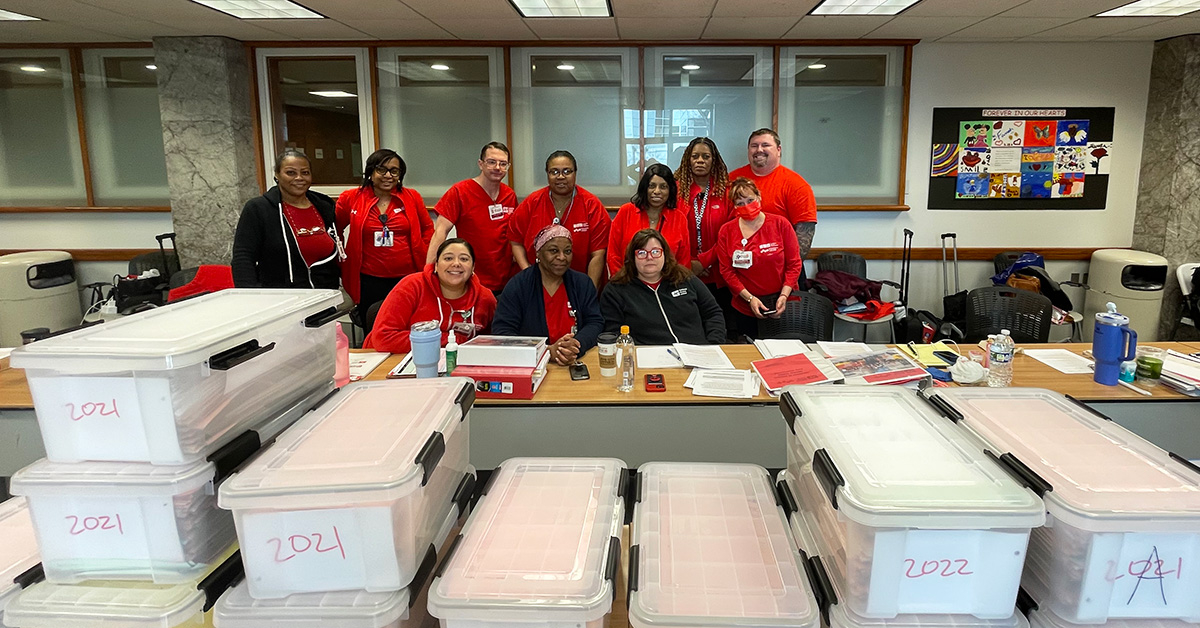 Group of nurses in red, smiling, in meeting room behind stacks of ADO documents