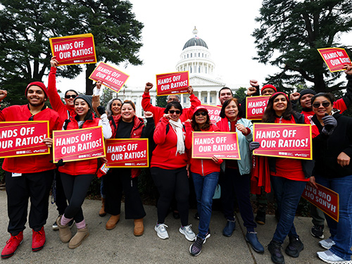 Group of nurses outside California State Capitol building holding signs "Hands Off Our Ratios"