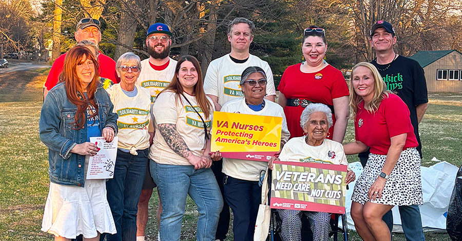 Group of nurses and veterans smiling, holding signs "VA Nurses Protecting America's Heroes" and "Veterans Need Care Not Cuts"