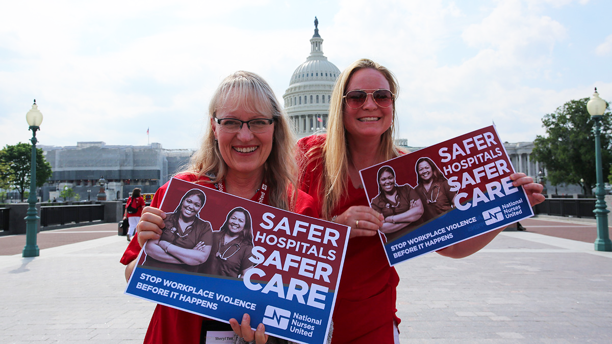 Two nurses in front of capitol holding signs 'Safer hospitals safer care: stop workplace violence before it happens."
