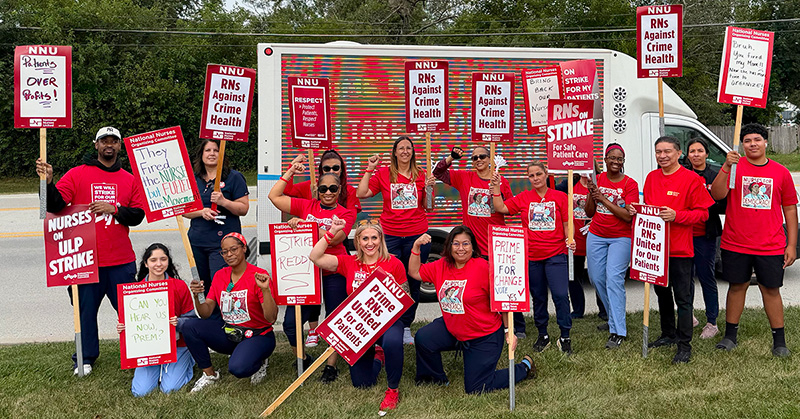 Large group of nurses outside holding picket signs "RNs Against Crime Health" and "RNs On Strike for Safe Patient Care".