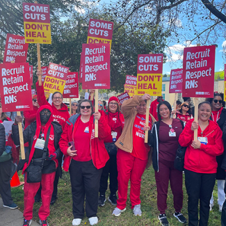 Large group of nurses on picket line, holding signs "Some Cuts Don't Heal" and "Recruit, Respect, Retain RNs"