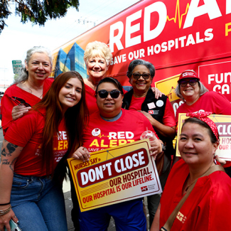 Group of nurses in front of Red Alert tour bus, smiling, holding sign "Don't close our hospital"