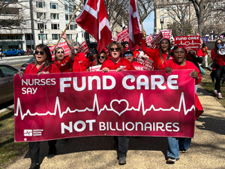 Nurses marching, holding banner "Fund Care NOT Billionaires"