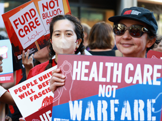 Nurse holding sign "Health Care Not Warfare"