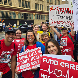 Group of nurses in No Kings march, holding signs "Fund Care, NOT Billionaires"