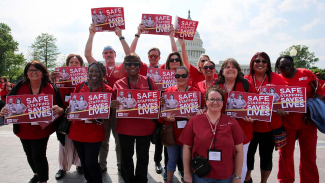 Large group of nurses in red, standing outside Capitol building in Washington, D.C., holding signs "Safe Staffing Saves Lives"