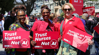 Three nurses smiling, holding signs "Trust Nurses Not A.I."