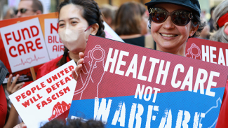 Nurse holding sign "Health Care NOT Warfare"