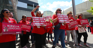 Nurses marching, holding signs "Some Cuts Don't Heal" and "Nurses for Democracy"