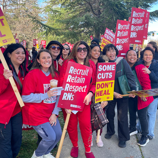 Nurses on picket line hold signs "Recruit, Retain, Respect RNs"