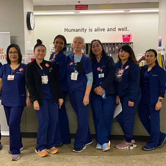 Group of eight nurses inside hospital, side-by-side, in blue scrubs