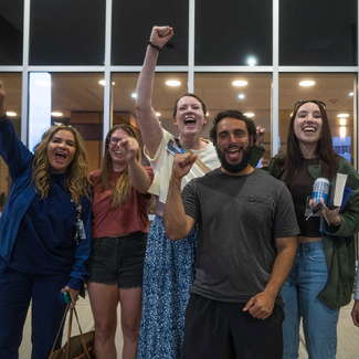 Group of six nurses outside hospital, smiling, with raised fists