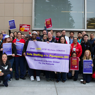 Group of nurses and physicians outside hospital holding banner "UCSF Workers Demand Safe Staffing"