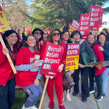 Nurses on picket line holding signs, smiling