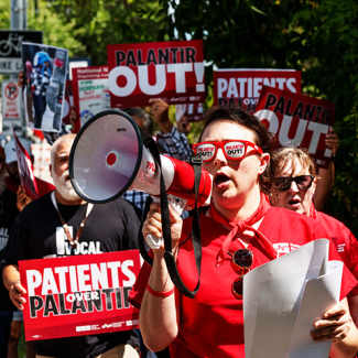 Marching folks with signs 'Palantir OUT!' and 'Patients over Palantir!"