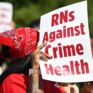 Nurse holding/shading herself with sign "RNs Against Crime Health"