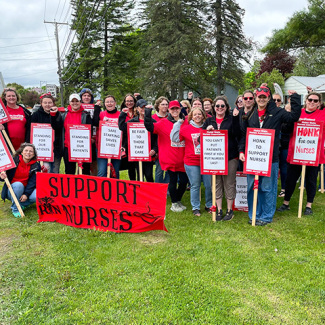 Large group of nurses outside, smiling, with raised fists, holding signs and banner "Support Nurses"