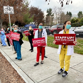 Group of four nurses outside hold signs "Staff up for safe patient care"