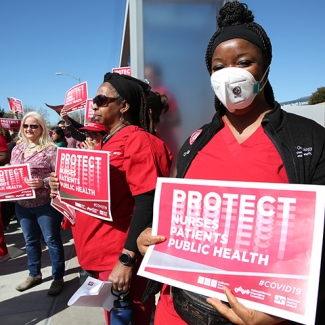 Nurses outside holding signs "Protect Nurses, Patients, Public Health"