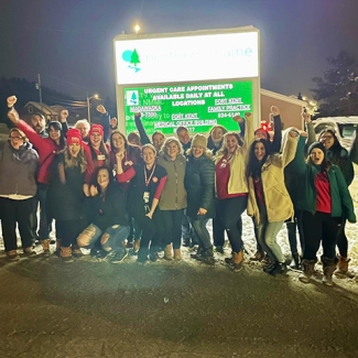 Large group of nurses standing outside hospital cheering with raised fists