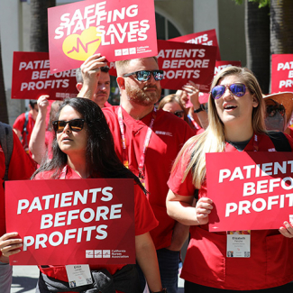 Nurses outside holding signs "Patients Before Profits" and "Safe Staffing Saves Lives"