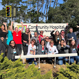 Group of nurses in front of hospital smiling, with raised fists