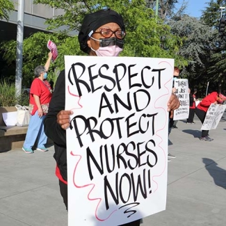 Nurse holds sign "Protect and Respect Nurses Now"