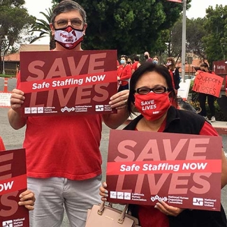 2 nurses outside hold signs "Safe Staffing Now"