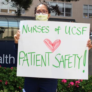 Nurse outside UCSF holding sign "Nurses of UCSF heart patient safety!"