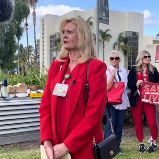 Nurse stands in front of TV camera, others stand behind 