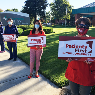 Nurses holding signs outside hospital "Patients first in the community"