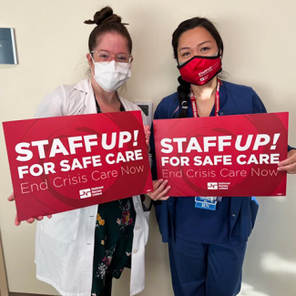 Two City of Hope medical staff holding signs "Staff up! For safe care. End Crisis Care Now"