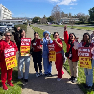 Group of nurses outside holding signs "Some Cuts Don't Heal"