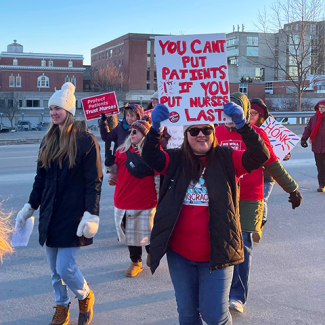 Nurses walking outside of hospital, one holding sign "You can't put patients first if you put nurses last"