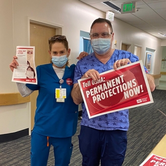 Two nurses inside hospital hold signs calling for permanent ETS