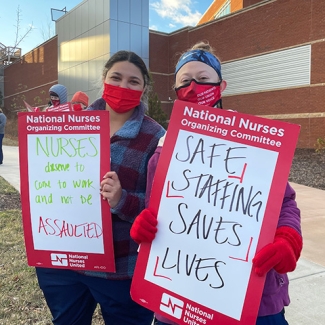 Two nurses outside holding signs calling for safe staffing and workplace violence prevention