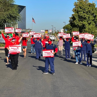 Large group of nurses outside hospital holding signs "Patients First"