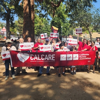 Large group of activists in park holding CalCare signs and banner