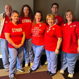 Group of seven nurses inside hospital smiling and wearing red